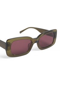 Olīvzaļas pārspīlētas saulesbrilles ar taisnstūra rāmjiem, tumši sarkaniem lēcu toņiem un gludu, spīdīgu apdari. Iekļauj izturīgas tempļus un caurspīdīgus akcentus.