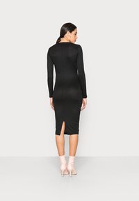 Vestido midi preto de manga longa com corte nas costas, design justo e textura suave, combinado com botas de tornozelo cor-de-rosa claro.