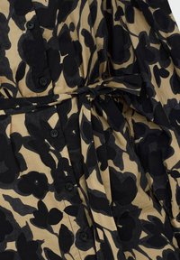 Robe beige avec motif floral noir, boutons noirs sur le devant et ceinture nouée à la taille.