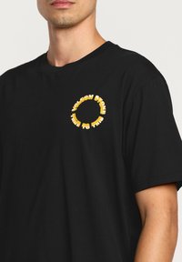 T-shirt en coton noir avec un graphique circulaire jaune portant les inscriptions "VOLCOM STONE" et "TRUE TO THIS", à manches courtes et à col rond.