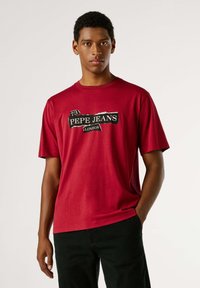 Camiseta roja de algodón con un estampado gráfico en blanco y negro que dice "73 PEPE JEANS LONDON." Manga corta y corte holgado.