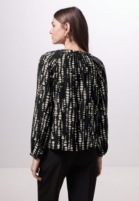 Blusa nera a maniche lunghe con un motivo a pois bianchi, scollo arricciato e polsini elastici. Abbinata a pantaloni neri.