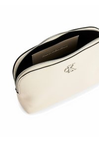 Borsa cosmetica in pelle beige con una texture liscia, chiusura a zip e hardware dorato. L'interno presenta una fodera nera e un dettaglio con logo.