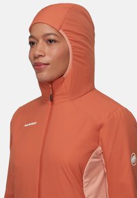 Huvjacka i orange med en slät yta, med framdragkedja och kontrasterande ljusrosa sidopaneler. Logotyp på vänster bröst och ärm.