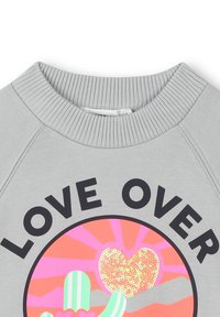 Sweatshirt gris avec encolure côtelée, affichant un graphique circulaire d'un cactus et d'un cœur pailleté avec le texte "LOVE OVER" au-dessus.