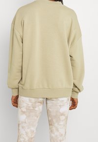 Sudadera de un beige claro con hombros caídos, puños y dobladillo acanalados. Textura suave. Combinada con pantalones claros y estampados que presentan un efecto de acuarela.