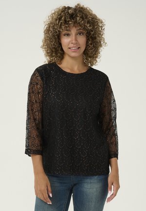 Black lace top with three-quarter sleeves, featuring a swirling pattern and a round neckline. Worn over denim jeans.