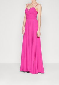 Robe maxi rose avec bretelles spaghetti réglables, corsage ajusté et jupe plissée fluide, en tissu léger et doux.