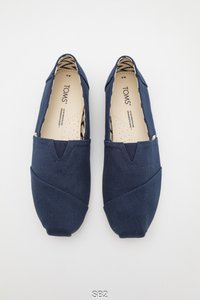 Marineblauwe canvas instapschoenen met een laag profiel, voorzien van diagonale stikseldetails en een gevoerde binnenkant van patroonstof. TOMS-logo aan de binnenzijde.