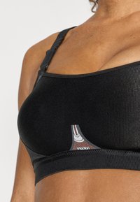 Sutien sport negru cu textură rigids, bretele reglabile și detaliu cu sigla în gri și roșu în față. Prezintă un design fără cusături pentru confort.