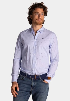 Lichtblauw overhemd met knopen en kleine, verspreide patronen. Lange mouwen en een kraag. Gepaard met blauwe jeans en een geweven riem.
