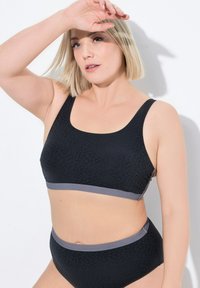 Musta bralette, jossa on hillitty leopardikuosi ja harmaa elastinen nauha; yhteensopivat korkea vyötäröiset alushousut, joissa on sama muotoilu ja värimaailma.