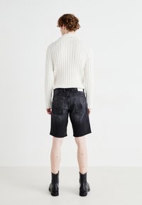 Suéter blanco de canalé, pantalones cortos de mezclilla negros con un acabado desgastado, bolsillos traseros visibles y botas de cuero negras, todo mostrado desde atrás.
