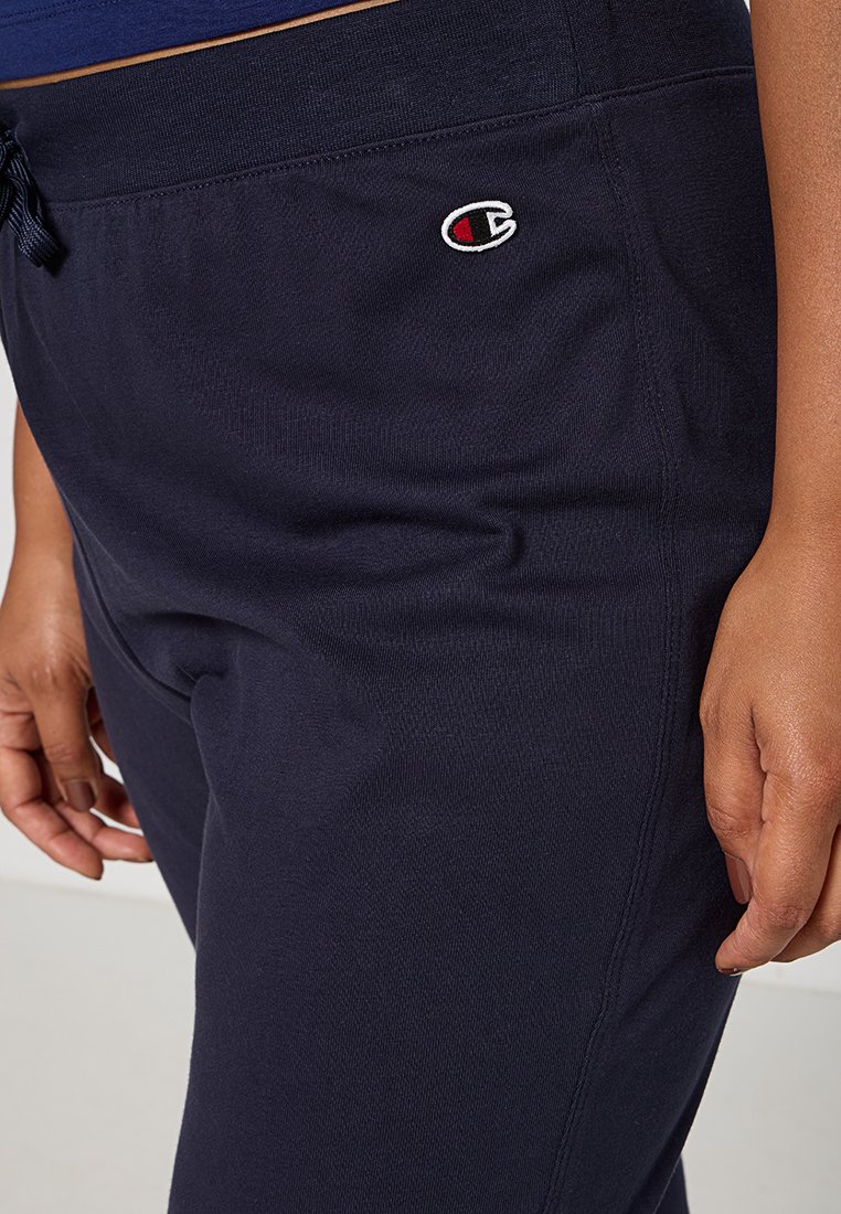 Marineblaue Baumwoll-Sweatpants mit einem Kordelzugbund, die ein kleines gesticktes Logo an der Seite und einen glatten, strukturierten Stoff aufweisen.