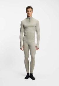 Jasnoszary termiczny komplet bazowy składający się z długiego topu z półzamkiem i otworami na kciuki, w połączeniu z dopasowanymi legginsami.