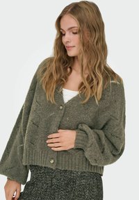 Cardigan verde lavorato a maglia con scollo a V, maniche oversize e orlo a costine. Presenta una chiusura centrale con bottoni e tessuto testurizzato.