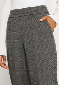 Pantalons à carreaux gris avec un tissu texturé, taille élastique et poches latérales. Le motif présente un mélange de petits et grands carreaux.