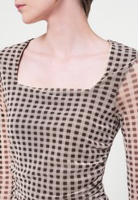 Top transparent cu decolteu pătrat, având un model în carouri maro și bej, cu laterale plisate și un material ușor, texturat.