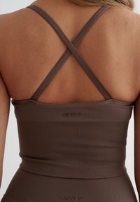 Bruine geribbelde sporttop met kruislings straps en een aansluitend ontwerp, met een logo op de achterkant. Textuurmateriaal verbetert de grip.