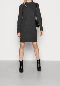 Robe en tricot grise à manches longues, coupe droite, ourlet côtelé et fente latérale. Associée à des bottes de cheville noires et un sac à bandoulière noir.