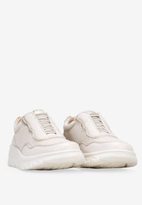 Zapatillas blancas tipo slip-on con paneles de malla perforada, acentos de cuero texturizado y cordones elásticos. Suela de goma gruesa con un patrón de relieve detallado.