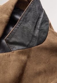 Barna szarvasbőr anyag texturált fekete béléssel. A gallér sima felületű, kontrasztos varrással.