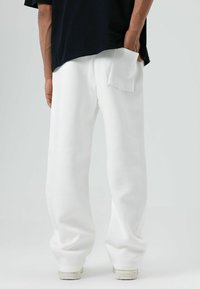 Witte, losvallende joggingbroek met een zachte textuur, voorzien van een achterzak en elastische boordjes bij de enkels. Gecombineerd met een zwart T-shirt.