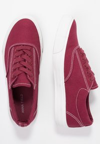 Scarpe da ginnastica in tela color bordeaux con lacci bianchi e suole in gomma. Cuciture a contrasto lungo i lati, design a taglio basso e imbottitura interna.