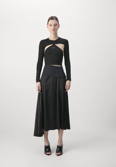Black long-sleeve top with cutout detail, paired with a flowing black skirt with an asymmetrical hemline. Glossy black open-toe shoes.