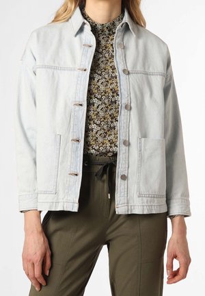 Femme portant une veste en denim bleu clair sur un haut à col montant à motif floral et un pantalon vert olive à cordon de serrage, vue du cou jusqu'aux hanches.