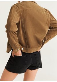 Brun kordjakke i velour med ribbet tekstur, featuring sølvknapper og en cropped design, parret med sorte denim shorts.