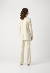 Completo a righe in colori pastello, con giacca aderente a una fessura e pantaloni svasati. Tessuto dalla consistenza morbida; dettagli hardware minimi.
