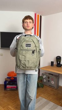 Zaļš mugursoma, kas izgatavota no neilona, ar priekšējo kabatu, sānu acs kabatām un regulējamiem siksnām, uz neitrāla fona.