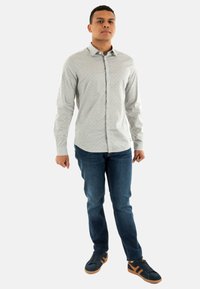 Chemise boutonnière gris clair avec de petits points multicolores, coupe ajustée, associée à un jean en denim foncé et des baskets bleu foncé avec des accents beige.
