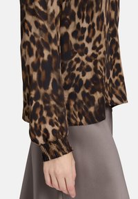 Leopardenmuster-Bluse aus leichtem Material, mit langen Ärmeln und gerafften Bündchen, ergänzt durch einen glatten, gedämpften grauen Rock.