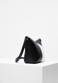 Borsa in pelle bianca e nera, design angolare con pannelli contrastanti, texture liscia, tracolla regolabile e dettaglio con cerniera laterale.