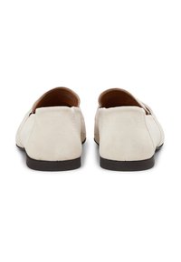 Beige suède loafers met een lage, donkere zool en gladde afgeronde achterkant, gekenmerkt door minimale stiksels en geen zichtbare hardwareaccenten.