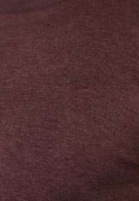 Primo piano di un tessuto in maglia color mogano con un delicato ricamo di testo in filo abbinato nella zona del petto.