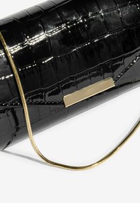 Mustekki musta keinonahkainen clutch, jossa on krokotiilitekstuuri, kultasävyinen ketjuhihna ja suorakulmainen kultainen yksityiskohta edessä.