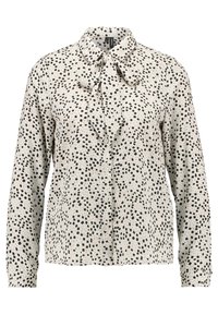 Blouse blanche à manches longues avec motif de carrés noirs irréguliers, boutons sur le devant et nœud noué au col.