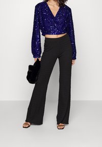Top corto a maniche lunghe in paillettes viola lucido abbinato a pantaloni neri a gamba larga e sandali neri open-toe. Inclusa borsa a pochette nera.