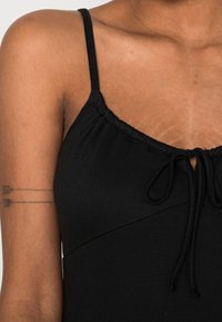 Top negro sin mangas con escote fruncido y detalle de cordón. Presenta una tela suave y un diseño ajustado y contorneado.