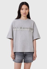 Grå oversized t-shirt lavet af bomuld med korte ærmer, prydet med glitrende "ALLSAINTS" tekst i rhinsten. Sammen med mørke denim shorts.
