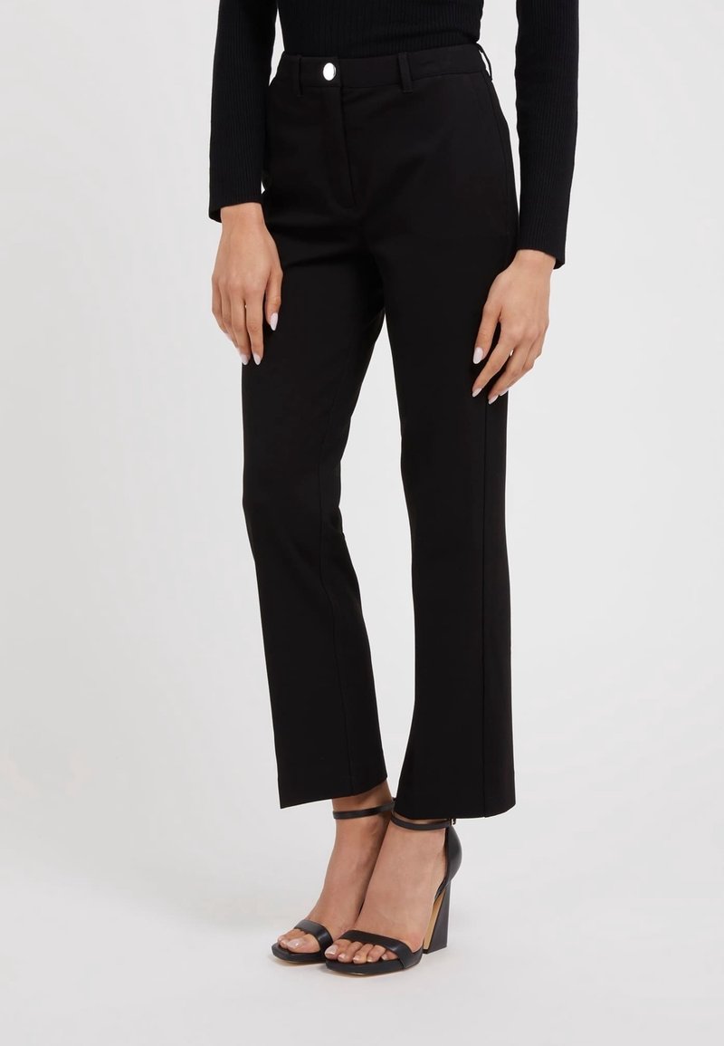 Czarne dopasowane spodnie o prostym kroju, z zamkiem błyskawicznym i metalowym guzikiem. Noszone z czarnymi sandałami na obcasie.