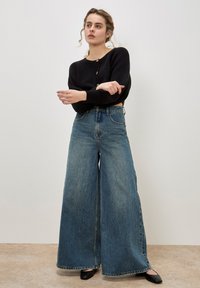 Hoge taille wijdeman spijkerbroek in lichtblauwe denim met een vervaagde afwerking, aangevuld met een zwarte geribbelde langemouw cropped trui.