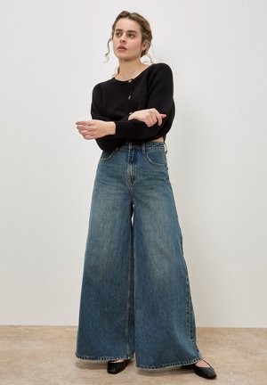 High-waisted wide-leg jeans in light blue denim with a faded finish, complemented by a black ribbed long-sleeve cropped sweater.