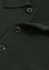 Tmavě zelené pletené polo tričko s límečkem a třemi černými knoflíky s květinovými výřezy, které vykazuje hladkou a vyrovnanou texturu.