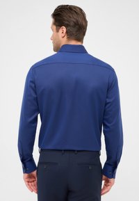 Marineblauwe langemouwen shirt met een gestructureerde afwerking, knoopmanchetten en een puntkraag, weergegeven vanaf de achterkant zonder zichtbare logo's.