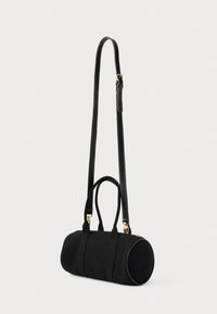 Μαυρη κυλινδρική τσάντα χειρός με κοντές υφασμάτινες λαβές και μακριά ρυθμιζόμενη δερμάτινη ζώνη με χρυσό υλικό σε απλό φόντο.