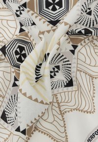 Λευκό ύφασμα με μαύρα, καφέ και μπεζ γεωμετρικά και αφηρημένα σχέδια, συμπεριλαμβανομένων εξαγώνων, κουκκίδων και κυματιστών γραμμών, ελαφρώς τσαλακωμένο.